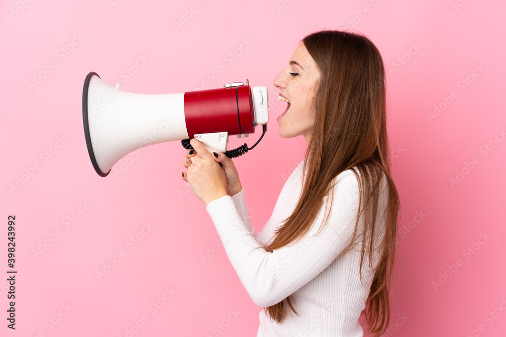 Young woman over isolated pink background shouting through a megaphone Young woman over isolated pink background shouting through a megaphone