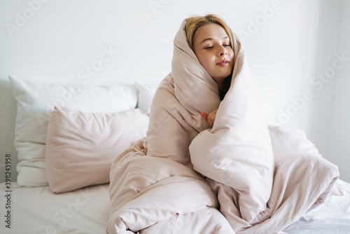 Beautiful pleased nice girl covered in blanket sitting on bed at home © Drobot Dean