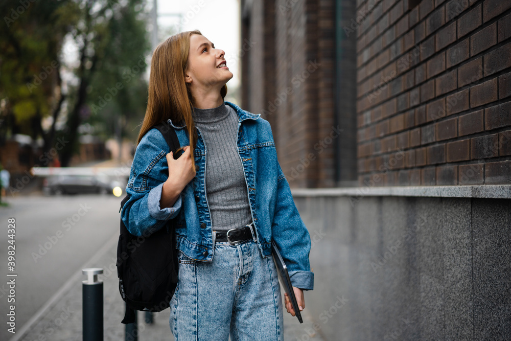 Beautiful happy student girl smiling and holding laptop while walking