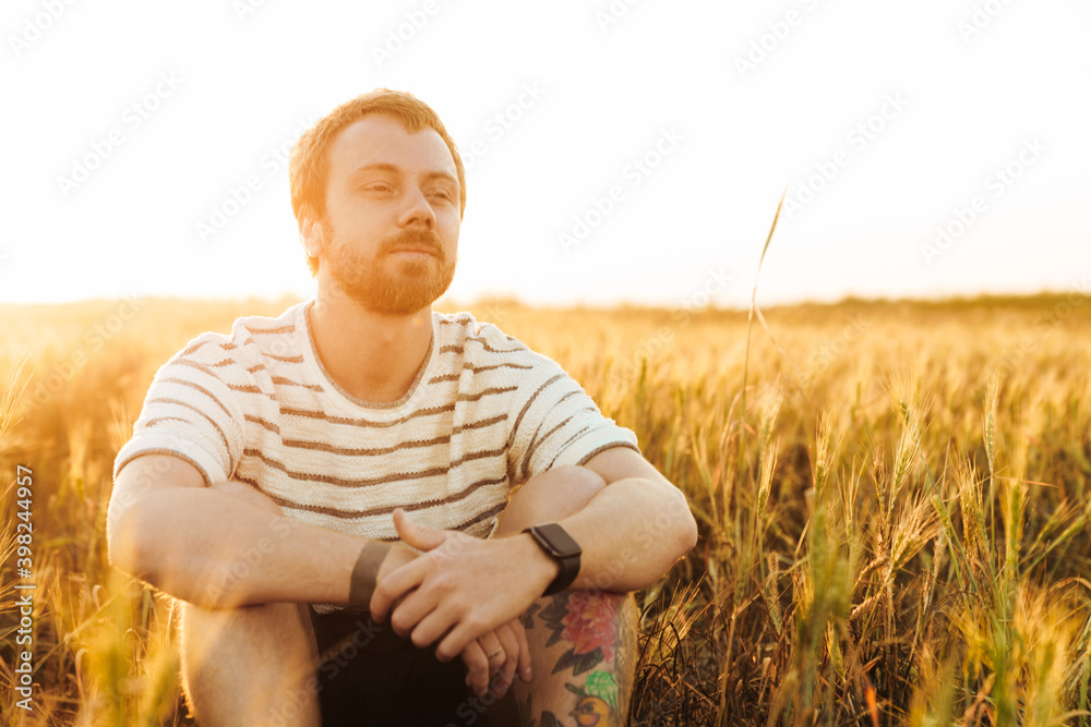 Serious young man sitting outside while looking aside Serious young man sitting outside while looking aside