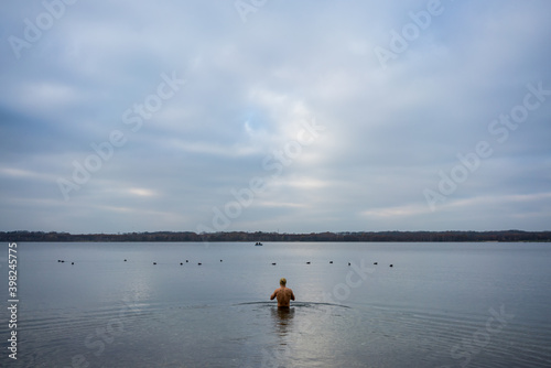 Man going into a lake to have a swim in cold water in autumn 