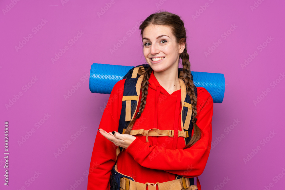 Young mountaineer girl with a big backpack over isolated purple background extending hands to the side for inviting to come Young mountaineer girl with a big backpack over isolated purple background extending hands to the side for inviting to come