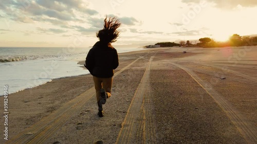 Ragazza corre sulla spiaggia con gli stivali al tramonto