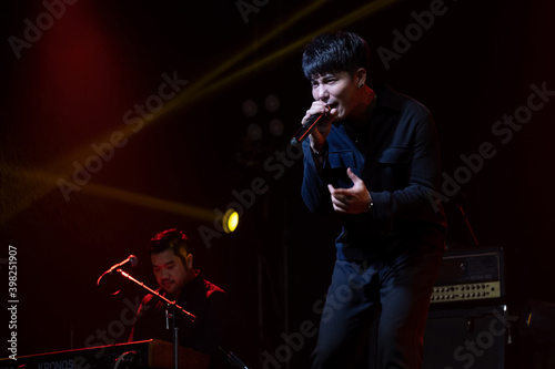 A man singing rock music on the stage with a red spotlight and behind background is microphone and drum. Feeling good on stage. Music and concert concept. Slight motion blur on performers.