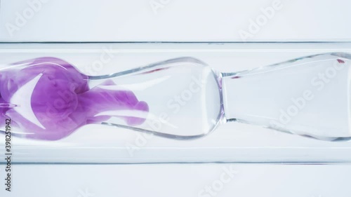 Pink liquid substance flows through a glass flask. Concept for advertising perfume and cosmetic products. Mixing pink ink with water in a large laboratory glass test tube.
