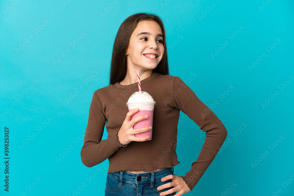 Little girl with strawberry milkshake isolated on blue background posing with arms at hip and smiling Little girl with strawberry milkshake isolated on blue background posing with arms at hip and smiling