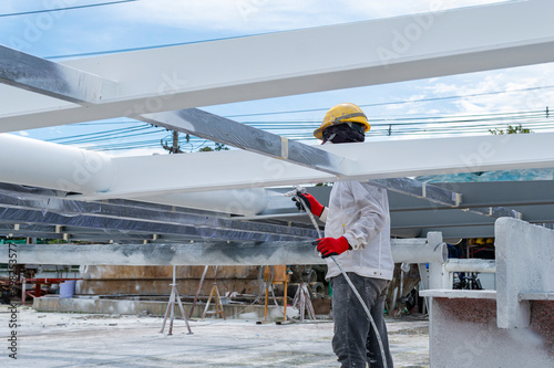 The painter is working to fireproof paint on steel structure with spray gun, at industrial factory.