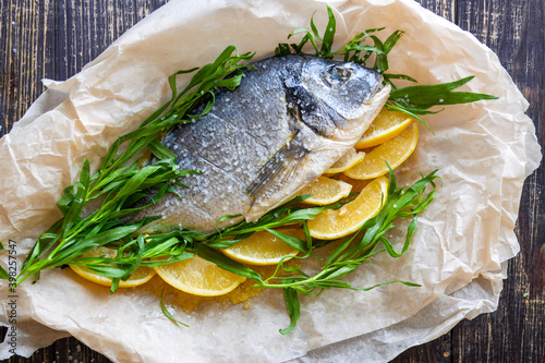Foto Fresh sea bream with lemon and herbs tarragon and dill on paper for baking