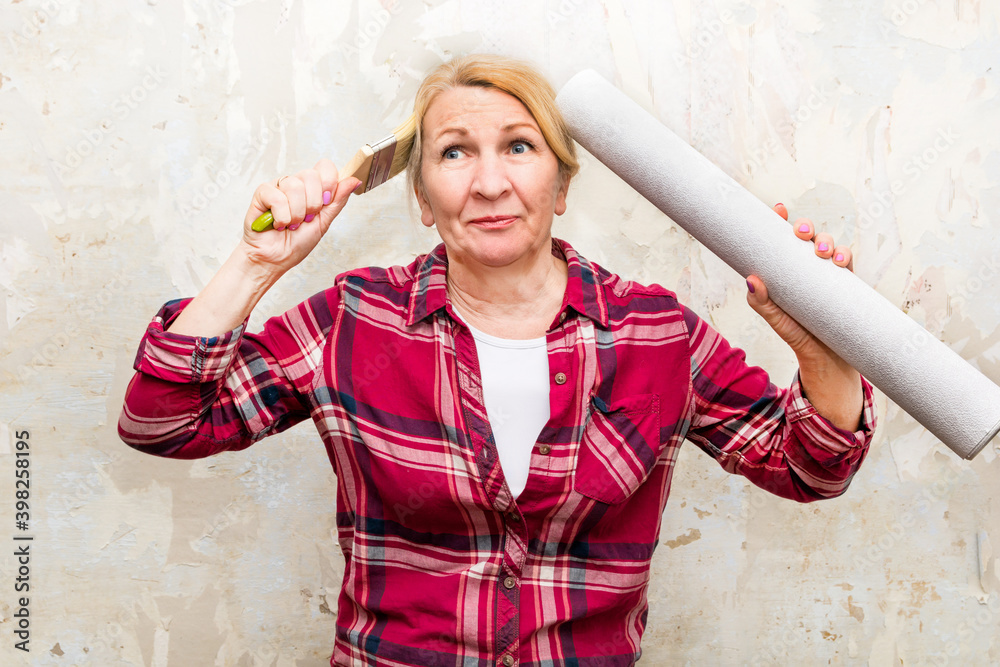 Against the background of an old wall, a woman stands with a brush and a roll of wallpaper in her hands. She thinks about how best to make repairs. DIY repair Against the background of an old wall, a woman stands with a brush and a roll of wallpaper in her hands. She thinks about how best to make repairs. DIY repair