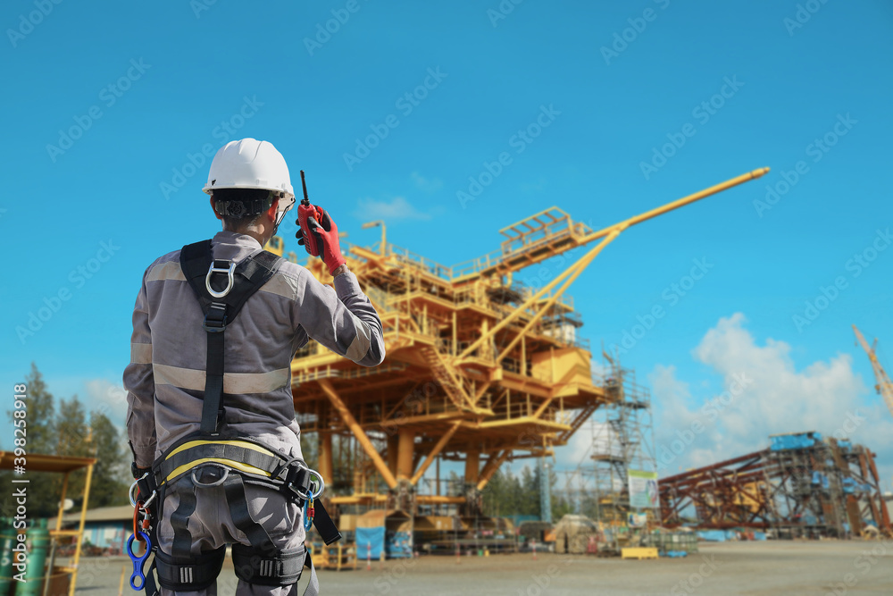 Workers wear with harnesses full body and hand holding walkie-talkie and lanyards for working at heights on rig drilling plant construction background with copy space for texture. Workers wear with harnesses full body and hand holding walkie-talkie and lanyards for working at heights on rig drilling plant construction background with copy space for texture.
