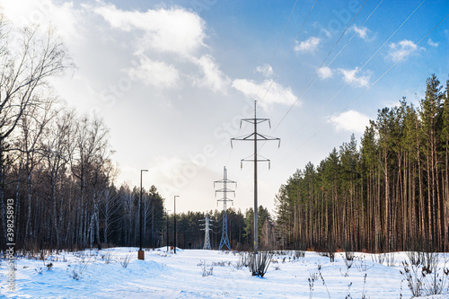 A high-voltage power line stands in the forest in winter under a blue sky