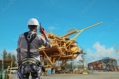 Workers wear with harnesses full body and hand holding walkie-talkie and lanyards for working at heights on rig drilling plant construction background with copy space for texture.