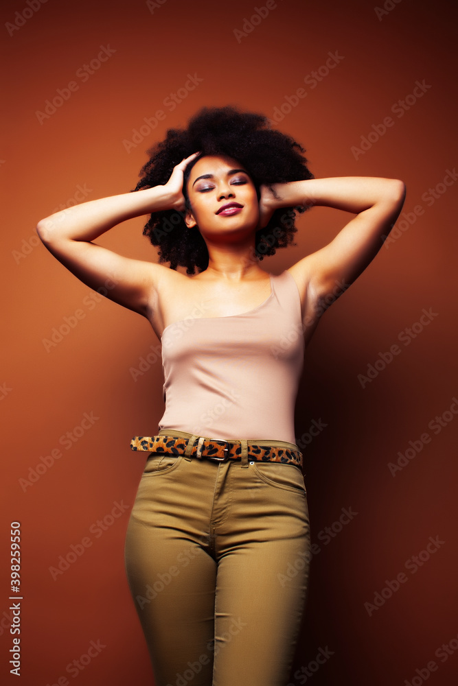 pretty young african american woman with curly hair posing cheerful gesturing on brown background, lifestyle people concept pretty young african american woman with curly hair posing cheerful gesturing on brown background, lifestyle people concept