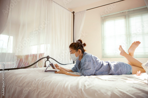 woman wearing protection mask reading message in computer tablet in home bed room