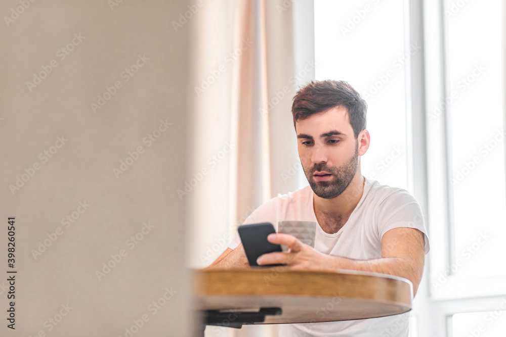 Photo of handsome young man using his smart phone while sitting on the couch at home.
