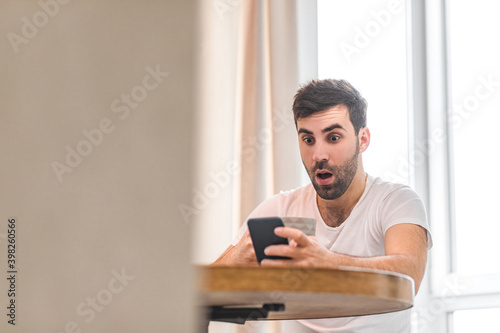 Photo of handsome young man using his smart phone while sitting on the couch at home.