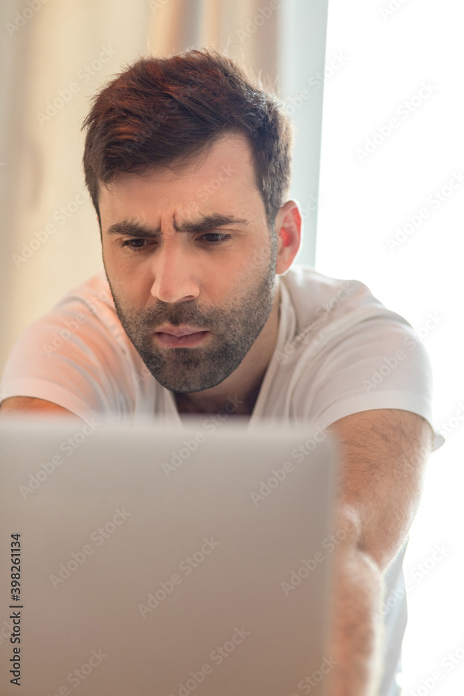 Photo of serious bearded man working on laptop while spending time at home. Photo of serious bearded man working on laptop while spending time at home.