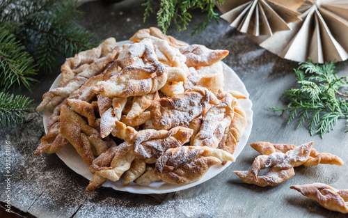 Brushwood hvorost russian traditional thin cookies with sugar powder on a white plate on wooden background with fir-tree branches. Selective focus