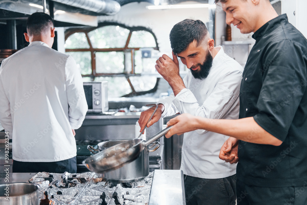 People in white uniform cooking food at kitchen together. Busy day at work People in white uniform cooking food at kitchen together. Busy day at work