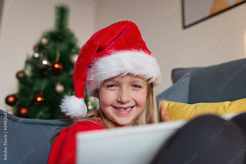 Cute blonde caucasian girl 7 years old sitting on couch near Christmas tree and writing letter to Santa Claus. Bedroom decorated with garlands. Xmas celebrate, happy new year 2021. Time to make wishes Cute blonde caucasian girl 7 years old sitting on couch near Christmas tree and writing letter to Santa Claus. Bedroom decorated with garlands. Xmas celebrate, happy new year 2021. Time to make wishes