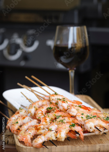 Grilled king prawns on skewers and glass of red wine. Background is a gas grill in bokeh