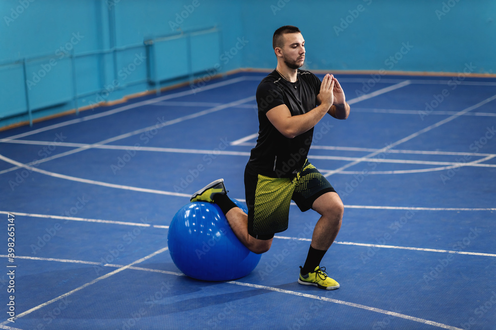 Sportsman in good shape doing lunges with pilates ball in sport hall.