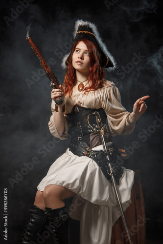 Young pirate female with long red hair. Woman is wearing a black corset bustier, tricorn hat , gun belt and armed with a pistol and sword.
