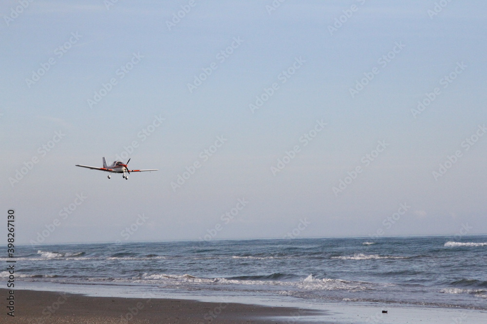 a small plane flying in the sky, with a remote control inside, very low over the sea, over water, waves