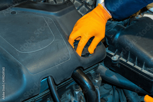 An image of a hand in an orange glove, unscrewing the oil plug of a car engine. © Максим Травкин