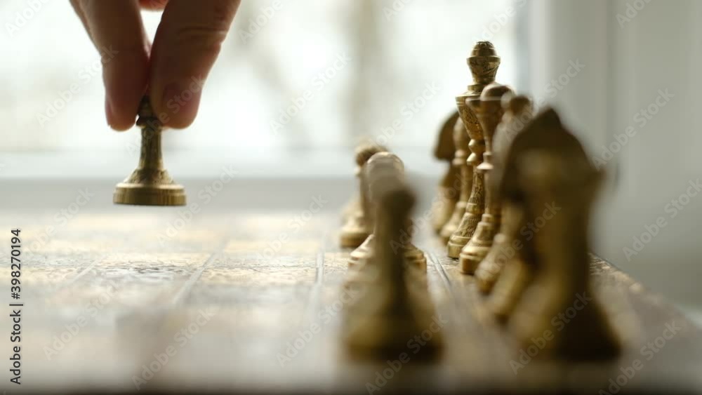 Close-up chess game. Metal chess pieces and the hand of a man who makes the first move with a pawn. The camera moves along the chessboard. UHD 4k video