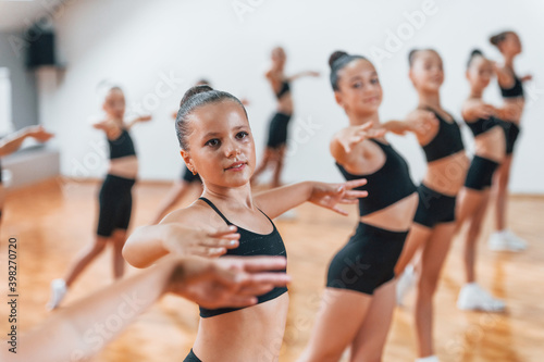 Standing and doing synchronised moves. Group of female kids practicing athletic exercises together indoors