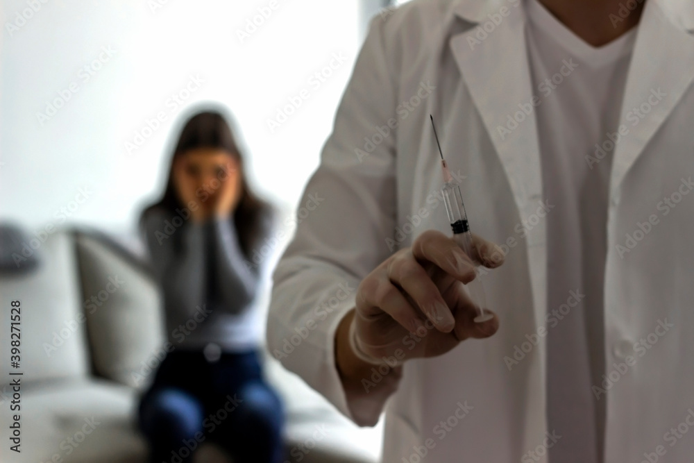 Photo of a recognizable male doctor hand,preparing syringe to injecting vaccine to female patient.Portrait of young male nurse holding injection with young patient in the background.Home care concept Photo of a recognizable male doctor hand,preparing syringe to injecting vaccine to female patient.Portrait of young male nurse holding injection with young patient in the background.Home care concept