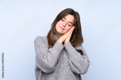 Teenager Brazilian girl over isolated blue background making sleep gesture in dorable expression © luismolinero