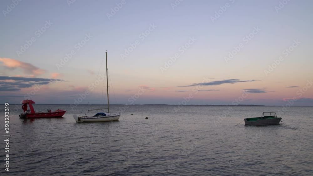 Fishing boats docked at the pier by the shore at sunset. Yachts on the water with colourful sunset sky in the background Fishing boats docked at the pier by the shore at sunset. Yachts on the water with colourful sunset sky in the background