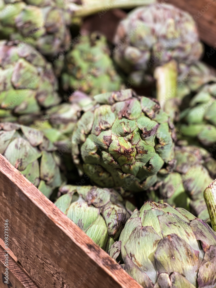 Fototapeta premium Artichokes for sale in farmers market or supermarket. Market hall. Presented in wooden box. Cynara cardunculus var. scolymus.