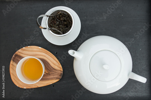 Tea set. Porcelain teapot  teacup with orange color hot water and fresh organic tea leaves in a metal filter. Beautiful professional top view shot of the teaset.