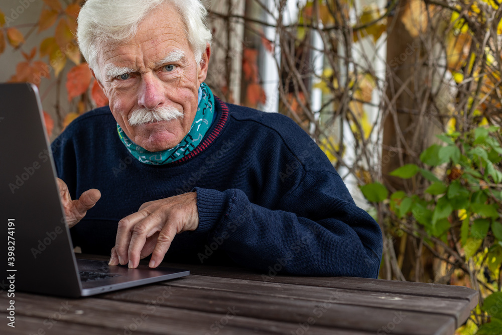 Senior man working on his laptop in the garden, thinking and looking at the camera. Senior man working on his laptop in the garden, thinking and looking at the camera.