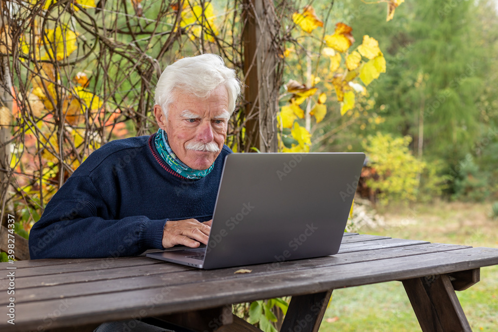 Old man working on laptop in his garden. A senior thoughtful man staring on the screen and making notes. Old man working on laptop in his garden. A senior thoughtful man staring on the screen and making notes.