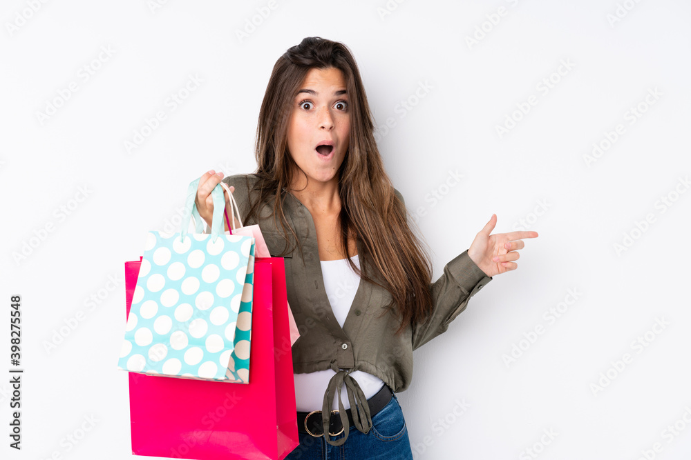 Teenager Brazilian girl with shopping bag over isolated white background surprised and pointing side Teenager Brazilian girl with shopping bag over isolated white background surprised and pointing side