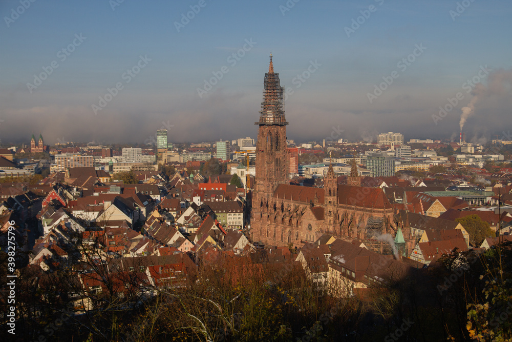 Freiburg im Breisgau, Germany - 11 09 2012: Scenic view to the city and the main church Munster from the mountain, snow-covered Black forest, mountains in the clouds. Early sunny winter morning