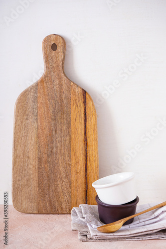 Wooden cutting board and kitchen utensils on a beige background. Close-up.