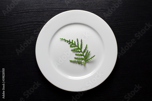 Vegetarianism, diet. A round, white plate with a green twig on a black wooden background.