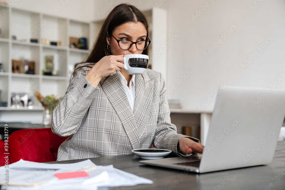 Serious woman drinking coffee while working with laptop and papers Serious woman drinking coffee while working with laptop and papers