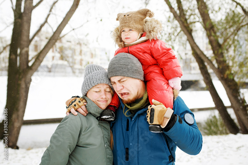 Portrait of funny happy family with one sad toddler in winter sporty outfit walking outdoors