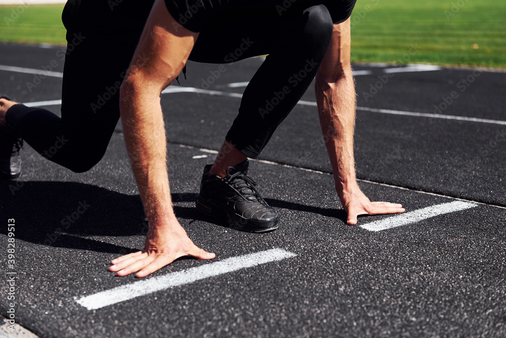 Runner is on starting position on track. Sportive young guy in black shirt and pants outdoors at daytime Runner is on starting position on track. Sportive young guy in black shirt and pants outdoors at daytime