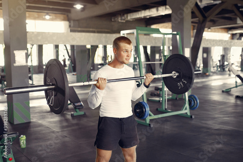 Sports man in the gym. A man performs exercises. Guy in a white blouse.