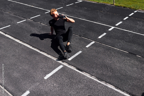 Tired runner sits on track and taking a break. Sportive young guy in black shirt and pants outdoors at daytime © standret