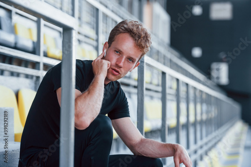 Free Download Listens to music when sitting. Sportive young guy in black shirt and pants outdoors at daytime - GFXLoad