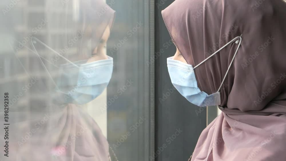 Side view of muslim woman with flu mask looking through window Side view of muslim woman with flu mask looking through window