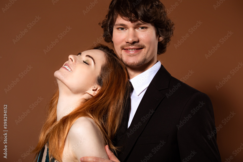 Beautiful red long hair style woman and handsome man with joyful smile celebrating new year holiday in fashion elegant clothes on orange bright background. Closeup
